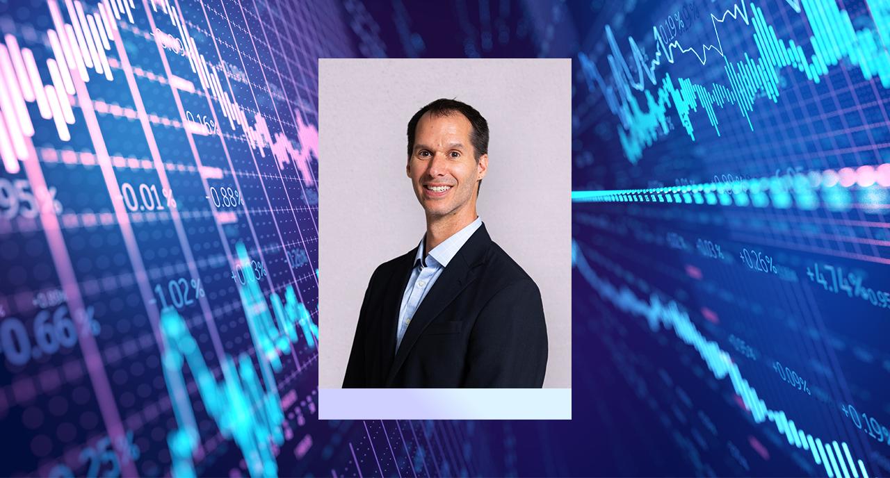 Photo of Eric Ludwig with stock market graphs behind him