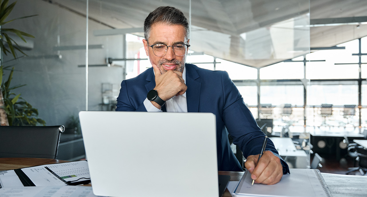 Middle aged man in a suit sitting at his desk smiling