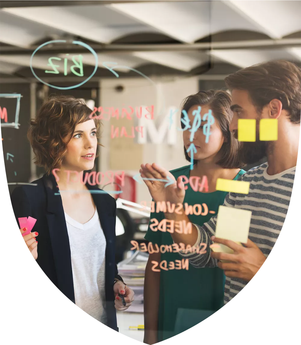 Three people working on a glass whiteboard