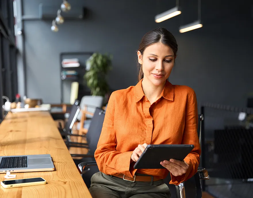 Woman in orange shirt typing on her iPad