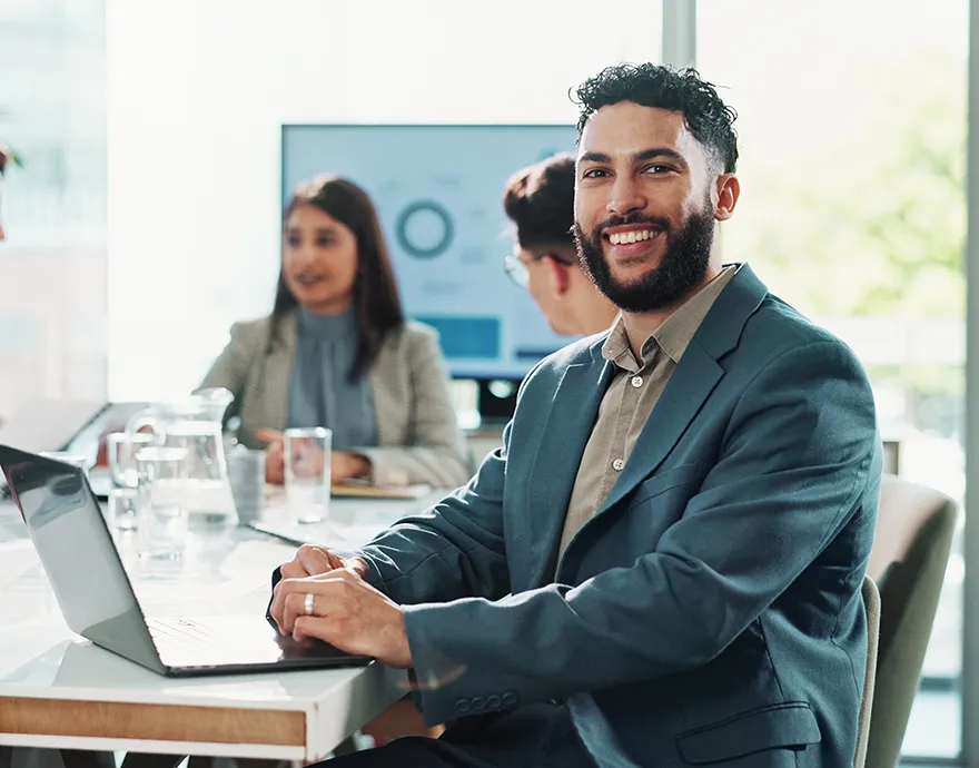 Man in a suit smiling while sitting in a work meeting