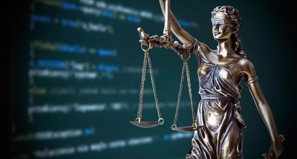 Statue of judge with scales in front of computer screen of code