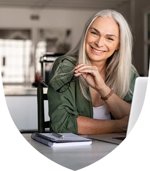 Close up of a woman holding her glasses and sitting at a laptop