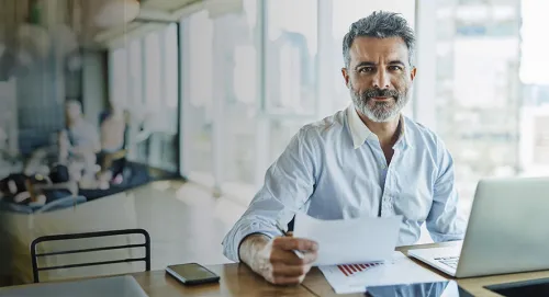 Elderly male advisor working at his desk with notes and a laptop