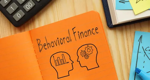 "Behavioral Finance" written on an orange notepad