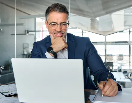 Middle aged man in a suit sitting at his desk smiling